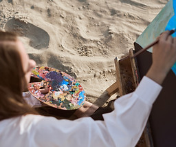 Young female artist paints on sandy beach, capturing vibrant colors of nature Serene seasi