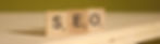 Wooden tiles with letters "S," "E," and "O" on a wooden surface, suggesting a word game. Blurred greenish background.