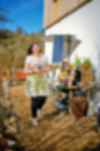 Eigentümerin in handbedruckter Blumenschürtze neben hözerner Tischdekoration vor dem Laden