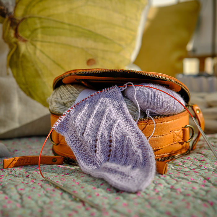 Gestricktes Projekt mit Nadeln in einer Vintage-Ledertasche auf einem gemütlichen Sessel.