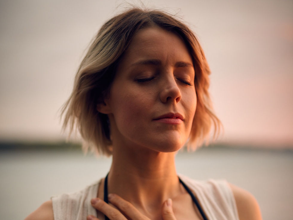 Woman with short hair in a bathing suit by the beach with eyes closed, calm look on face, and hand over heart