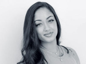 Bianca Lysette with long hair smiling softly, wearing a necklace and casual top against a plain background. Black and white photo.