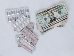 Blister packs of prescription pills next to a stack of U.S. dollar bills, representing the high cost of medications