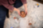 Baby lying on patterned rug, wearing a headband, gazing upward. Craniosacral therapist gently touch the baby's head. Playful, calm setting. photo: Kates Takes
