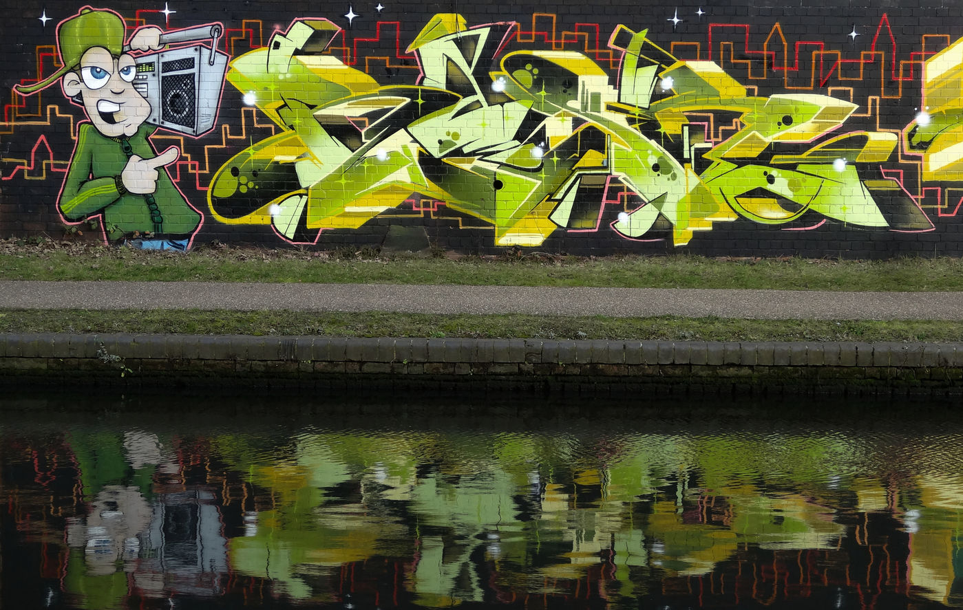 Graffiti wall featuring a character holding an old school ghetto blaster and letters painted by writer artist Rask HBR Hated But Rated crew
