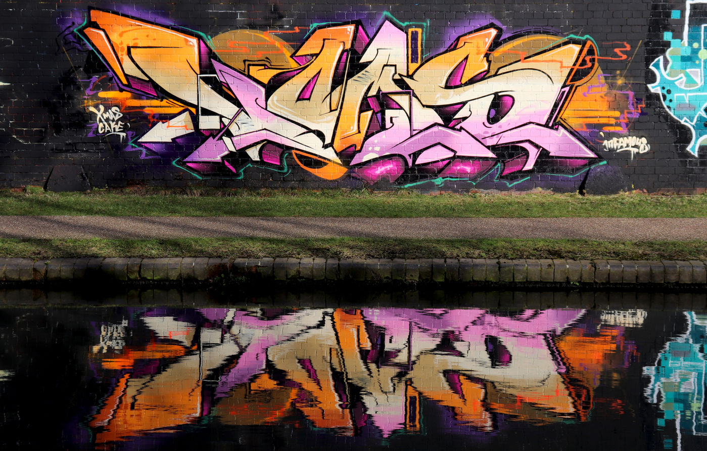 A reflection photograph of a piece of graffiti spray painted next to a canal
