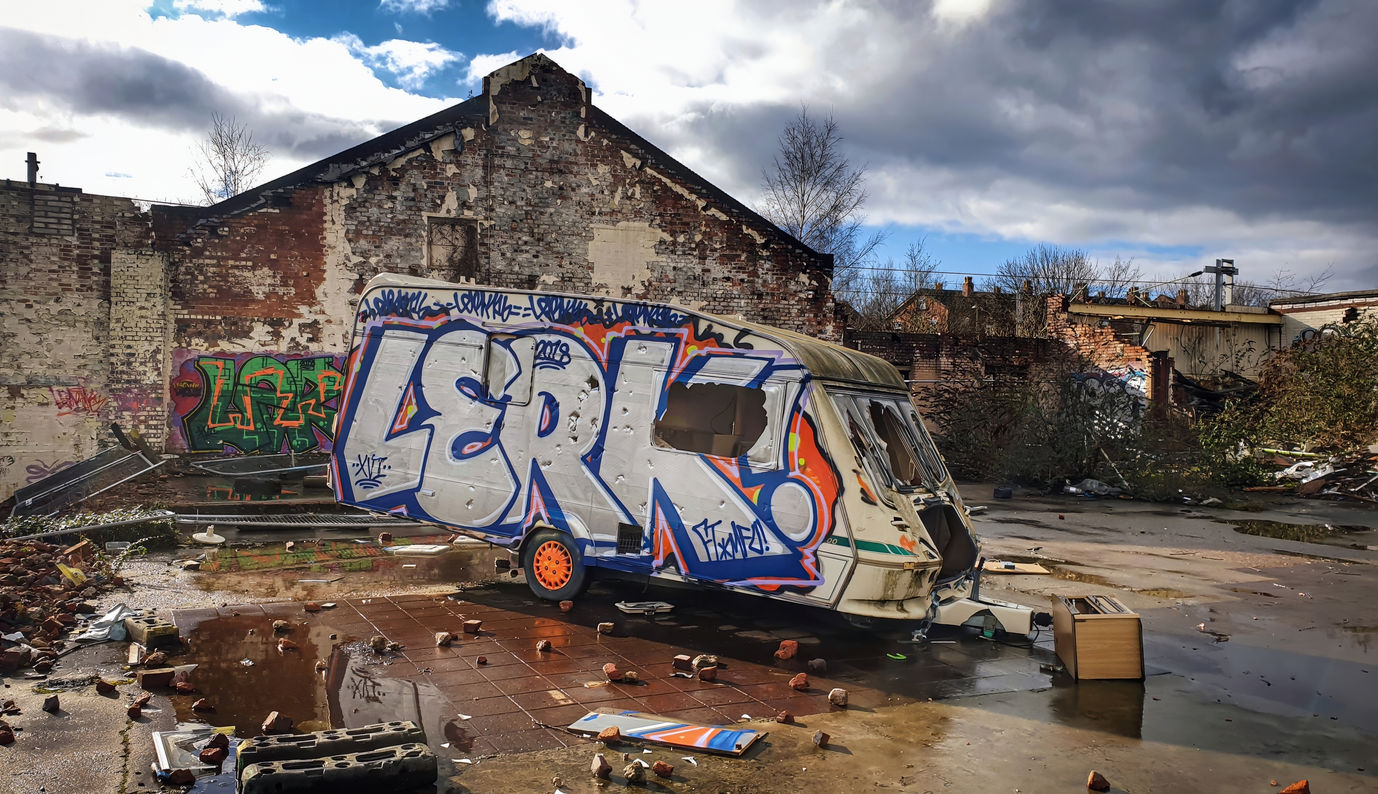 Silver or chrome graffiti letters on an abandoned caravan on some old dystopian looking wasteland with very dark and moody looking clouds above