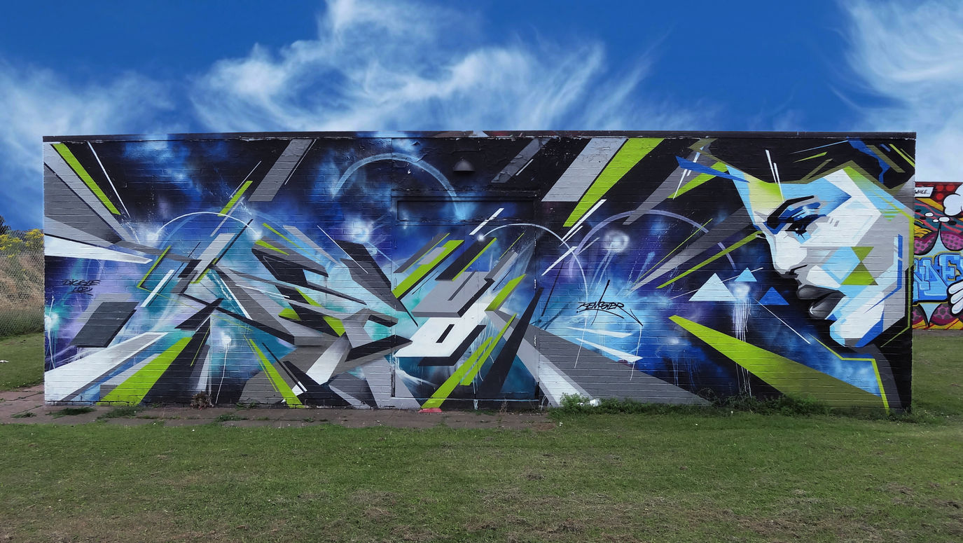 Abstract graffiti letters on wall with an abstract looking face to the right of the letters