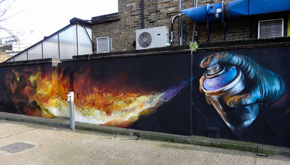 An amazing piece of street art show a gloved hand, that is holding a can, and it's shooting fire out of it.