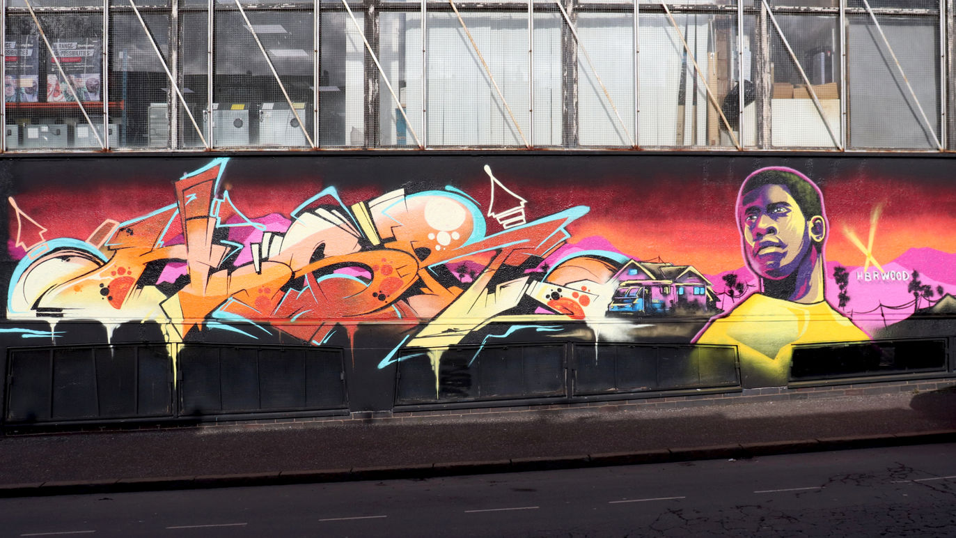Brightly coloured graffiti wall with a character of a black person next to it with the Hollwood sign in the background spray painted by the HBR Hated But Rated crew