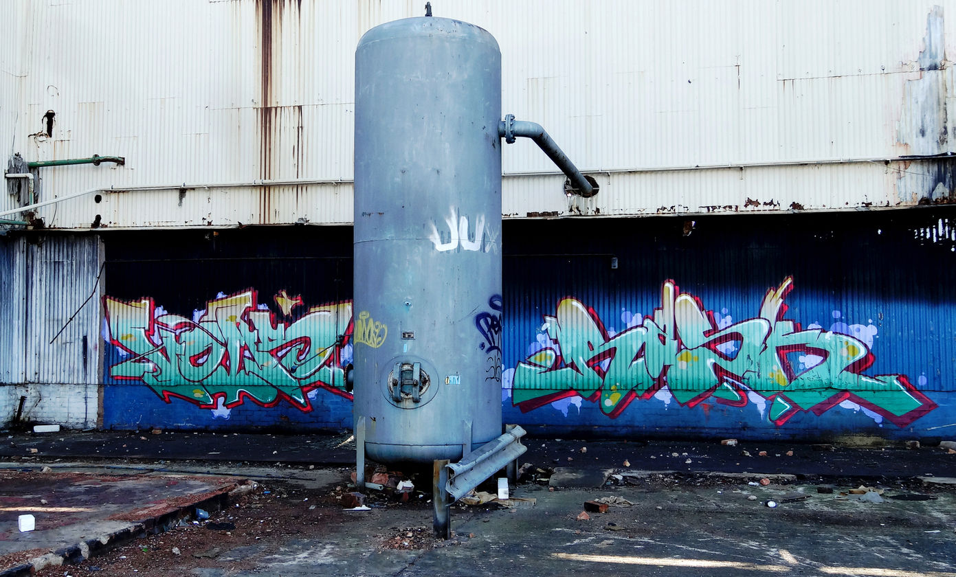 Graffiti letters, in a derelict location, with a water tank in the foreground spray painted by writer artist Voms NFA and Rask HBR