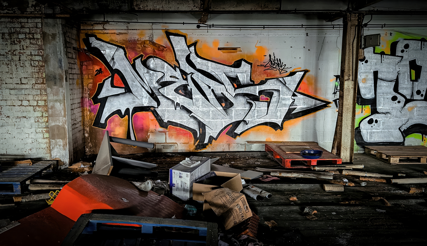 Silver and orange graffiti art, painted inside a derelict building, surrounded by wooden pallets by writer artist Meds Medik KG crew