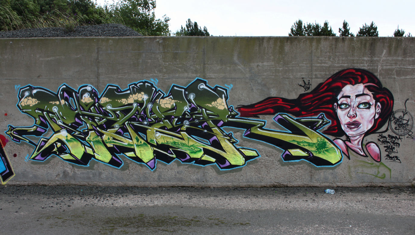 Green elongated graffiti letters, painted on a wall in a derelict quarry, featuring the face of a woman with red flowing hair