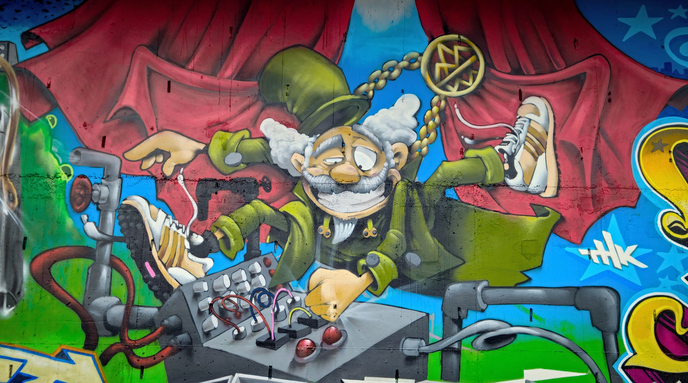 A crazy green coloured graffiti character wearing Adidas trainers and a gold chain
