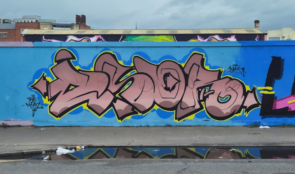 Pastel coloured graffiti letters painted on some boards with the artwork reflected in a puddle of water