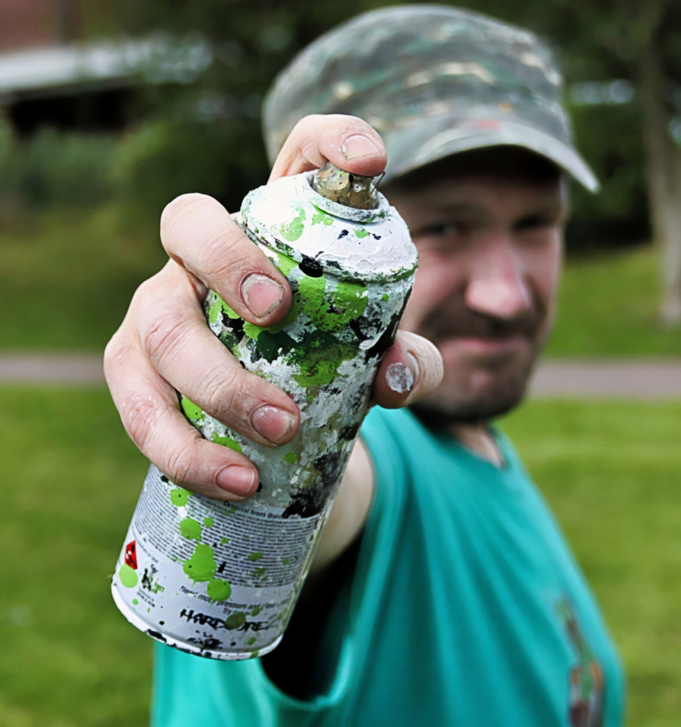 A photograph of a man holding a can of spray paint that is pointed directly at a camera lense