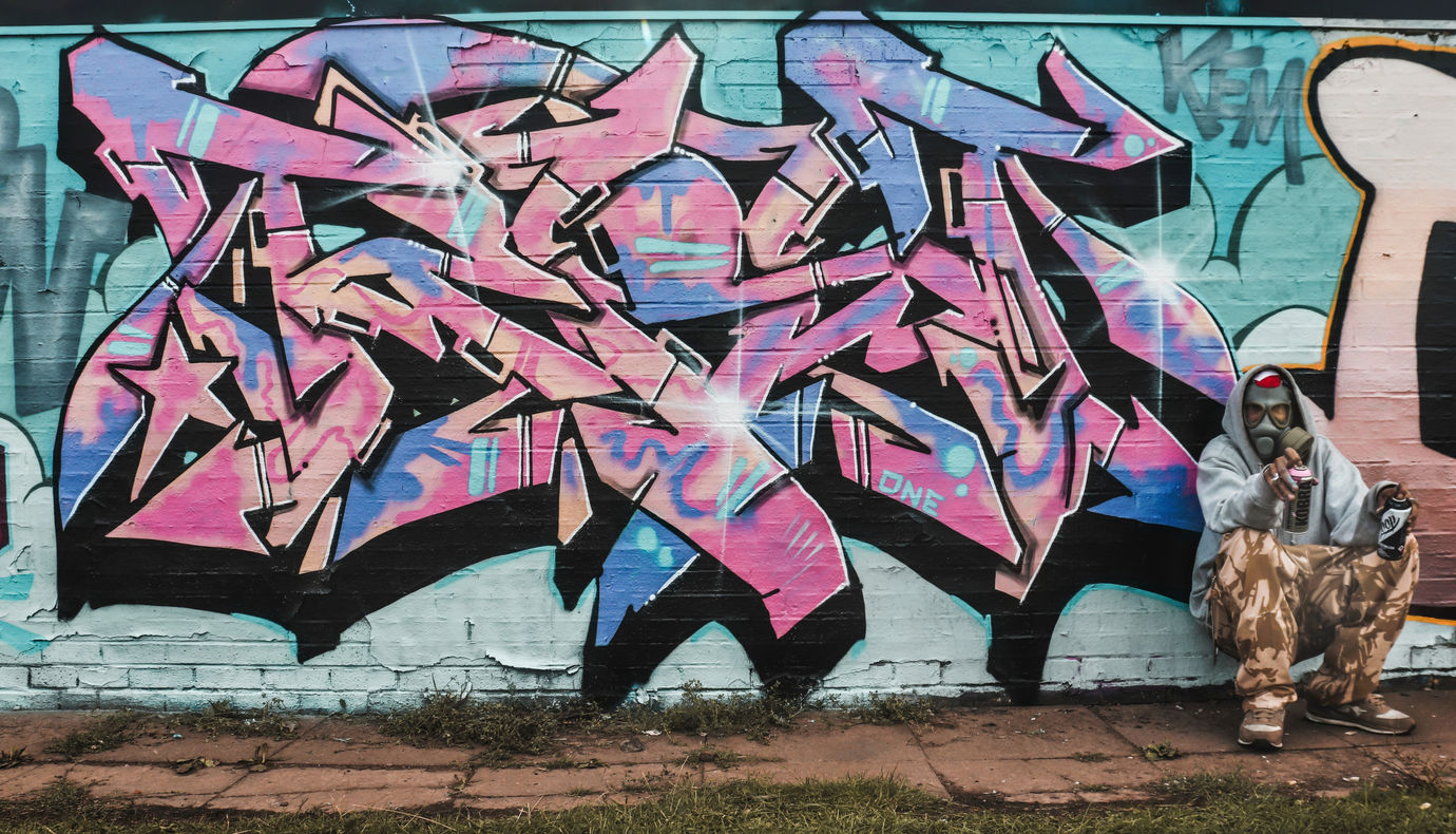 A graffiti artist posing in front of one of his pieces whilst wearing a gas mask