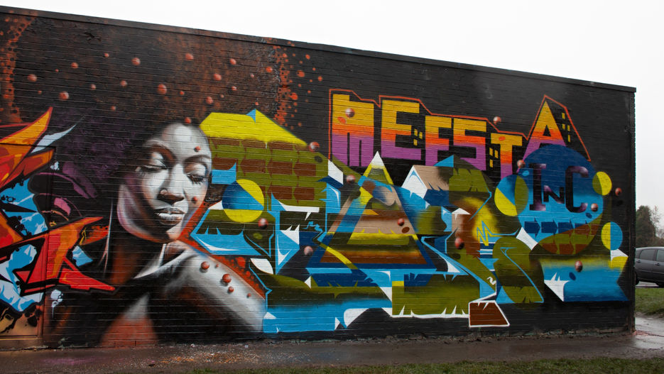 A colourful wall of graffiti lettering with a realistic image of a black woman next to it