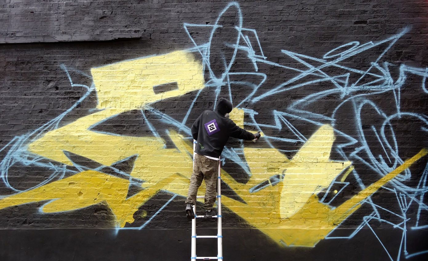 A graffiti artist, on ladders, spray painting a huge wall - the photo really shows the scale of the wall
