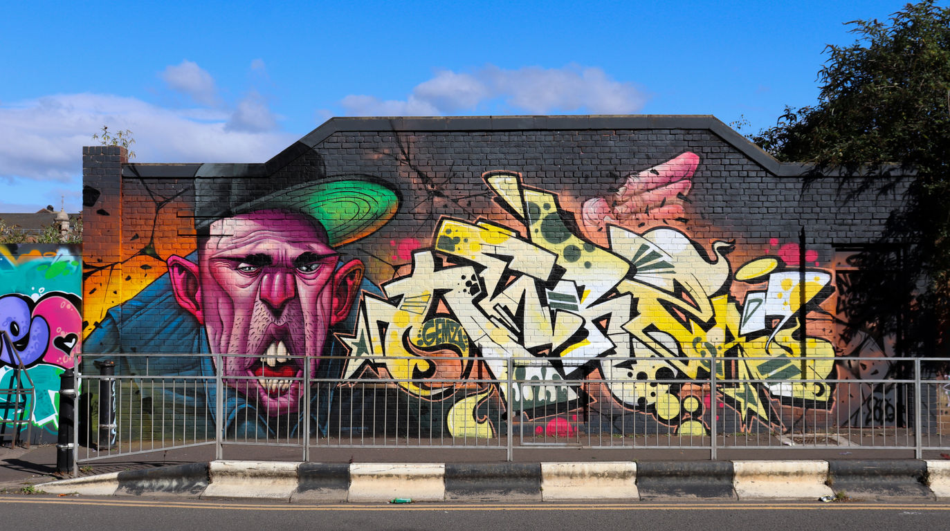 Yellow graffiti lettering next to a crazy character of a man, showing his teeth, and wearing a baseball cap