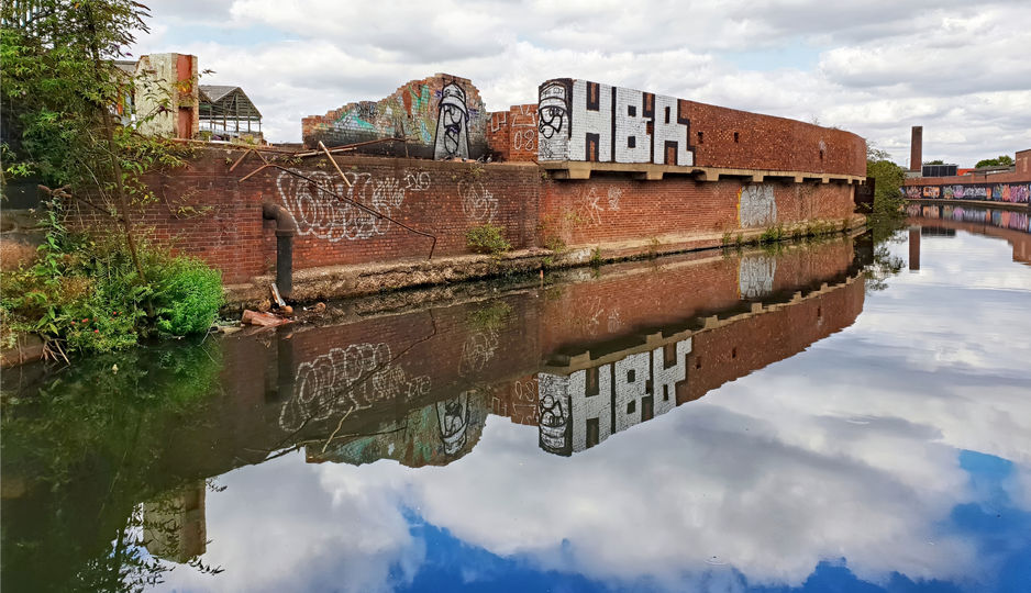 A wall that has some graffiti on it but the reflections of the clouds are amazing.