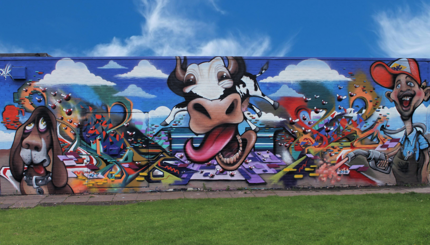 An insane graffiti wall featuring a flying cow, a basset hound dog and a petrol pump attendant