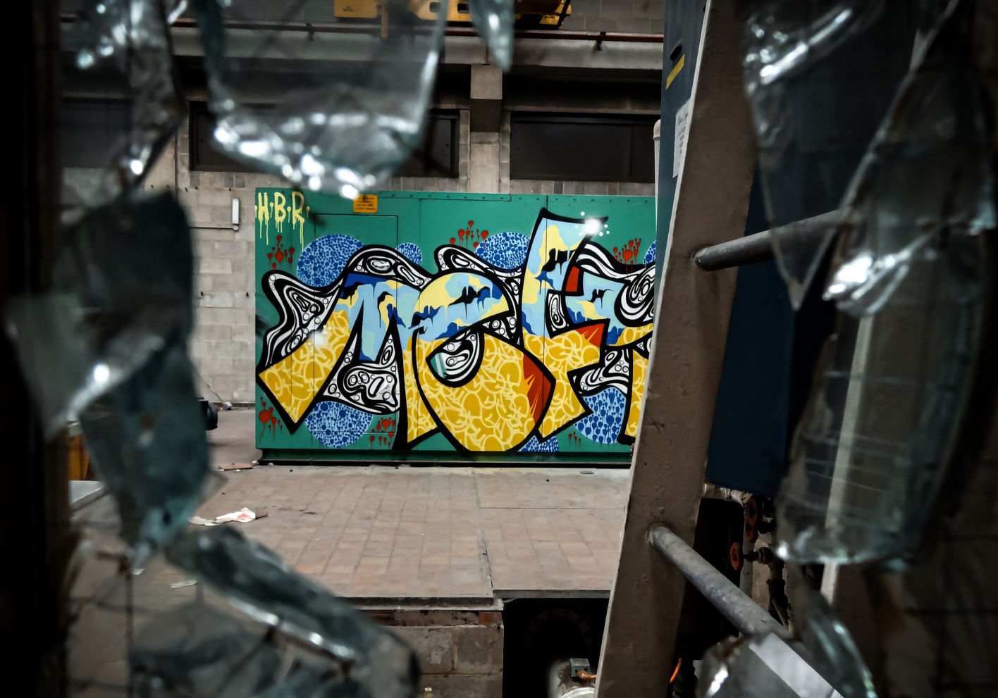 A photograph of one of the graffiti writer artist Mef Remo piece HBR Hated But Rated crew taken through some broken glass