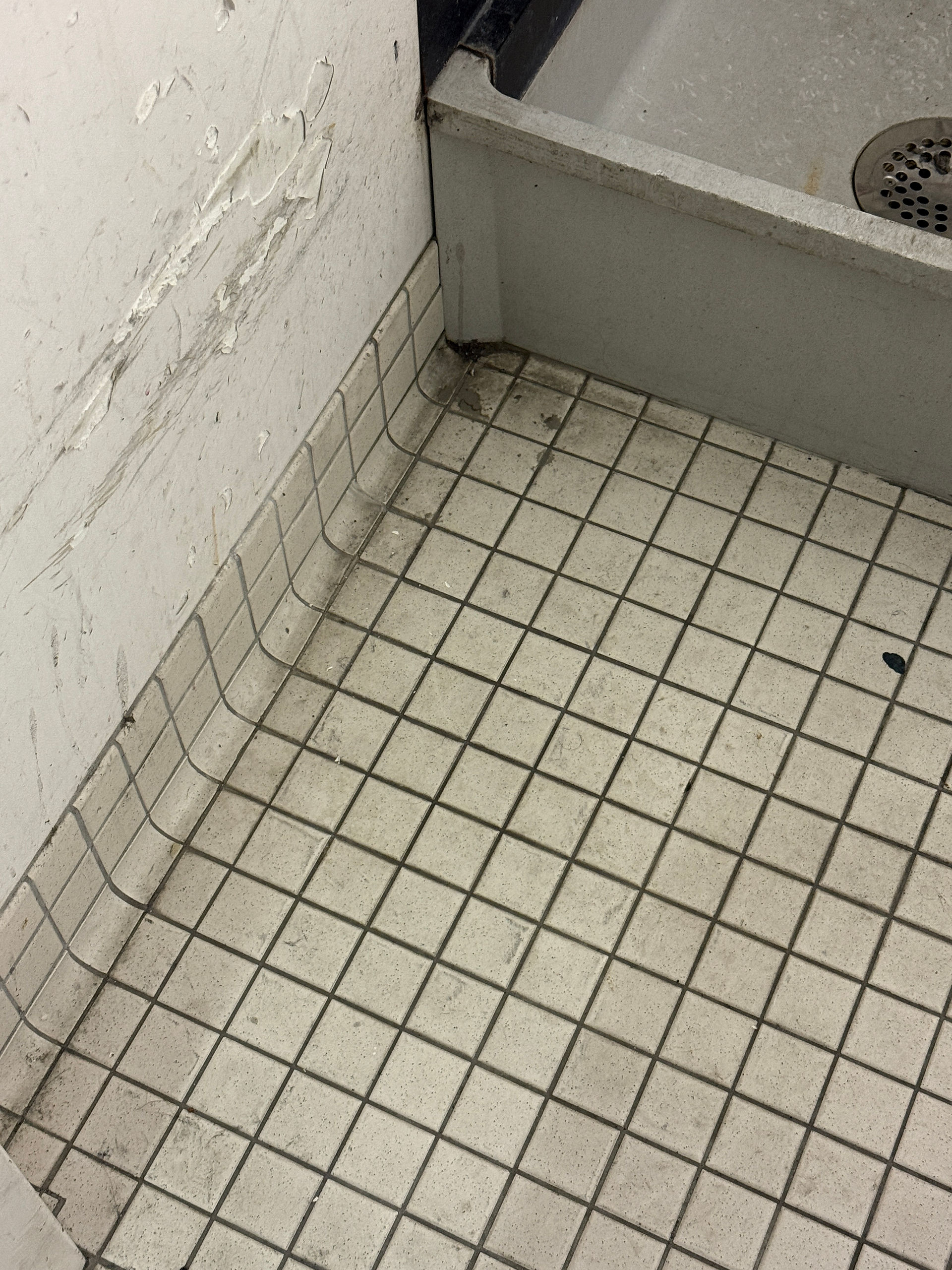 Coin d’une conciergerie montrant un plancher carrelé taché, des joints encrassés et un mur abîmé par l’humidité ou les frottements, illustrant un manque d’entretien et d’organisation du local d’entretien ménager.