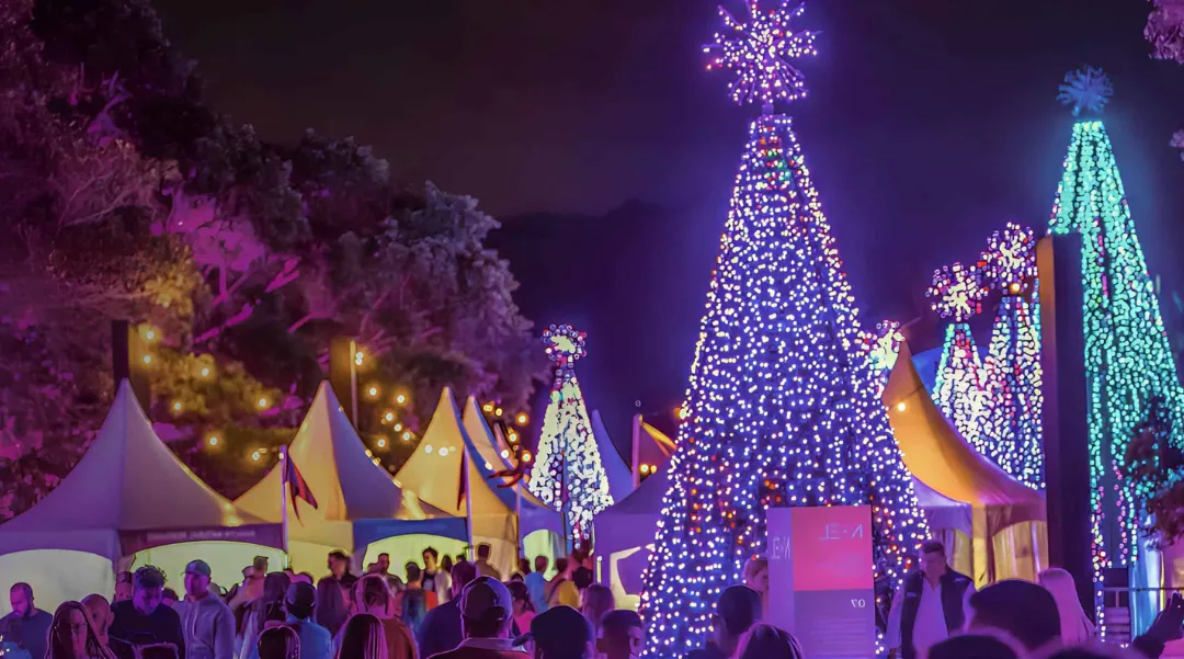 Brightly lit Christmas trees and decorated tents at a festive night event, evoking joy and celebration.