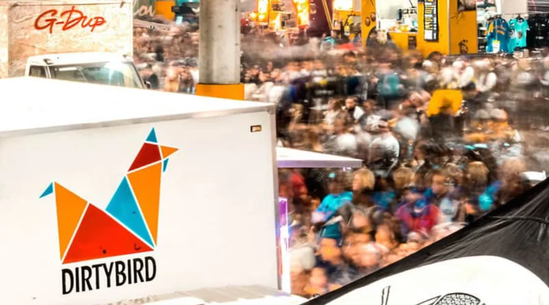 A vibrant crowd at a festival with the Dirtybird logo visible on a food truck, showcasing a lively event atmosphere.
