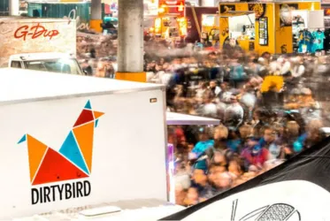 A vibrant crowd at a festival with the Dirtybird logo visible on a food truck, showcasing a lively event atmosphere.