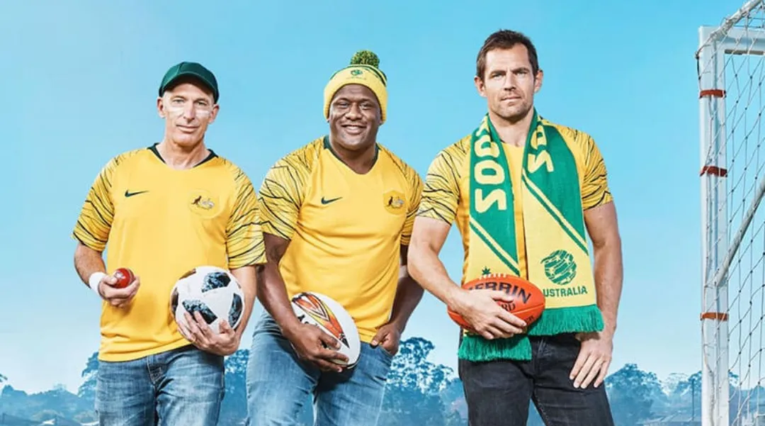 Three men in Australian sports jerseys holding balls, celebrating national sports culture and team spirit.