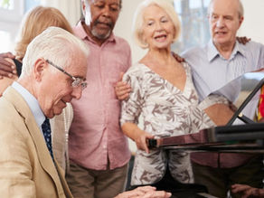 Picture of a group of elderly friends signing along to a piano.