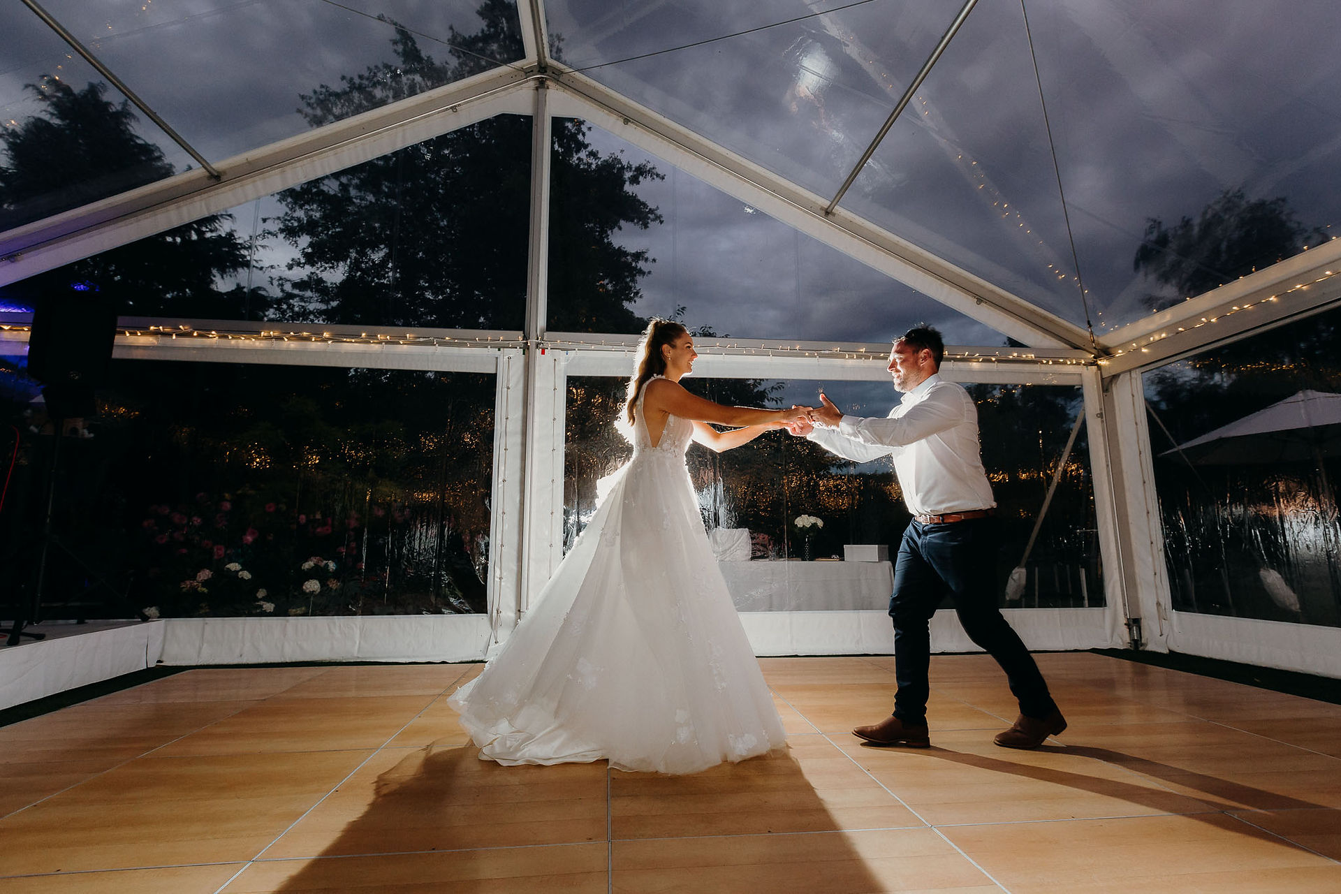 Bride and groom sharing their first dance beneath a clear marquee