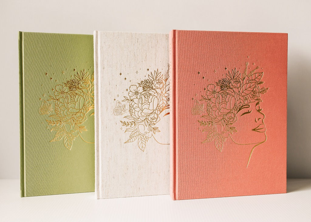 FRONT HARDCOVER OF THE JOY JOURNAL WITH GOLD FOIL DESIGN ON FRONT SHOWING 3 BOOKS IN COLOUR SAGE, OATMEAL AND BLUSH.