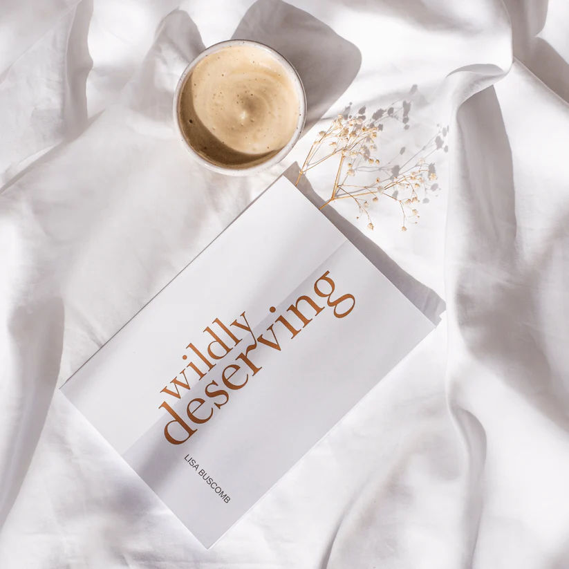 white book with coloured font on a bed with a cup of coffee in the sun