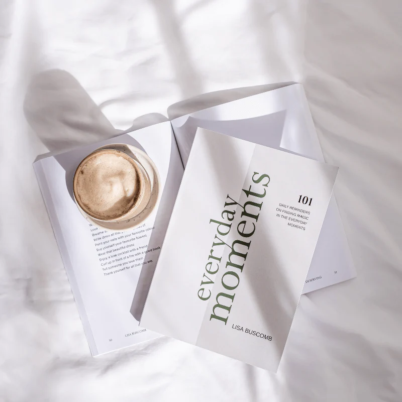 white book with green coloured font with a coffee in the sun on a white bed