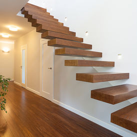 Floating wooden staircase with indoor plant, wood floors, and white walls.