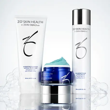 A range of Zo Skin Health products are displayed on a white countertop. The products include cleansers, toners, and moisturizers, with their individual packaging visible. The background is white with bubbles.