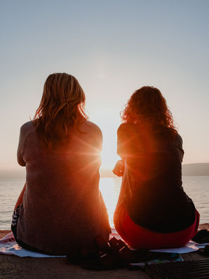 Two people sitting together watching a sunset at the end of summer, reflecting on seasonal transitions and managing end-of-summer stress.