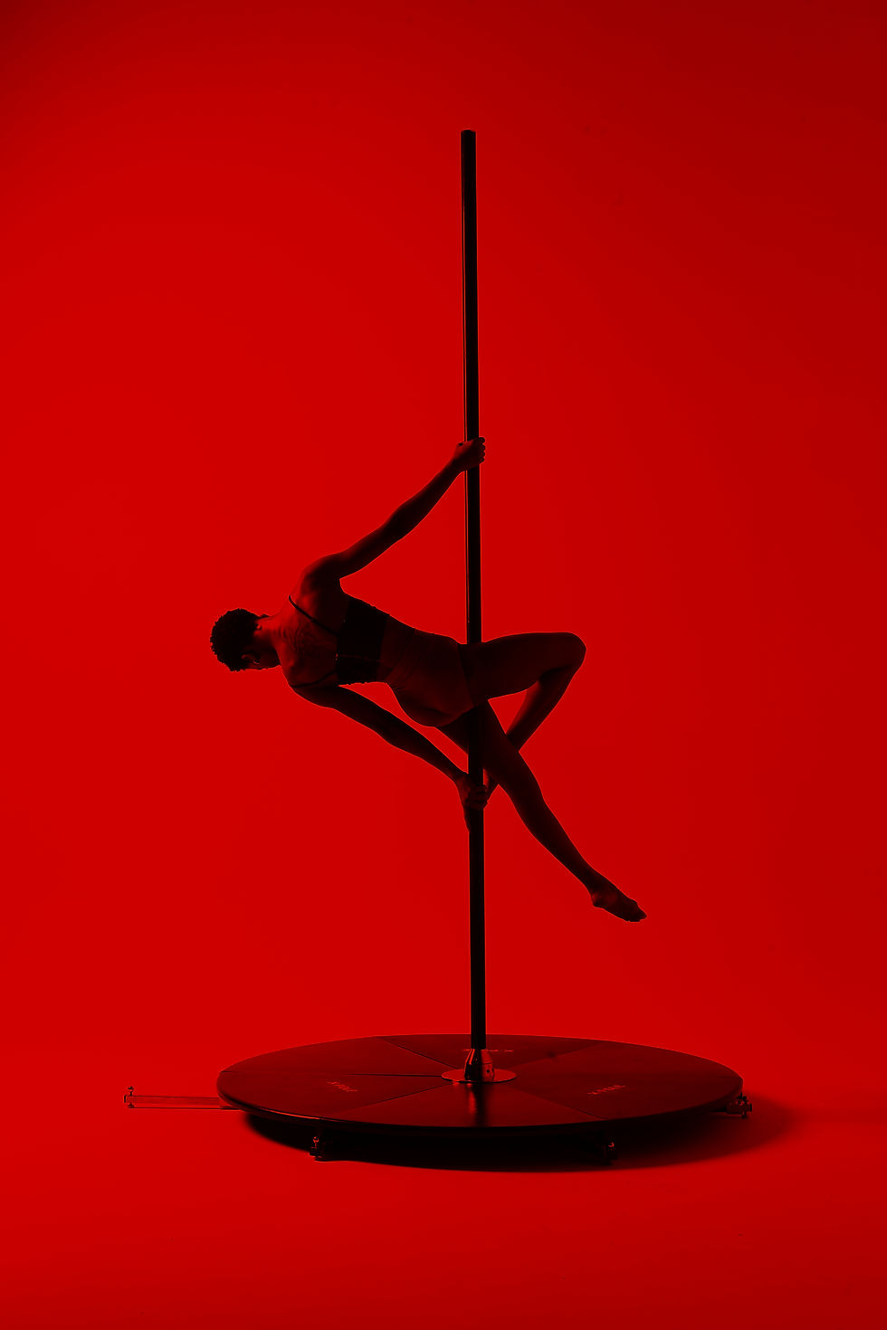 A dancer gracefully performs a pole routine against a dramatic red backdrop, showcasing strength and elegance.