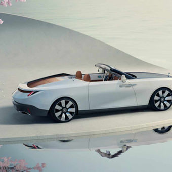 Convertible Rolls Royce Drop tail car parked on a light concrete surface beside a reflective water body. Pink blossoming tree nearby. Calm and serene mood.