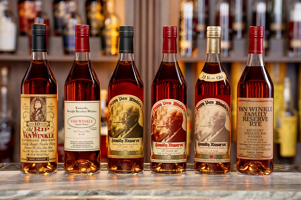 Bottles of Pappy Van Winkle bourbon are lined up on a wooden surface against a blurred bar backdrop. Labels detail different ages and types.
