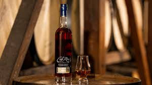 Bottle and glass of dark liquor on a wooden barrel in a dimly lit cellar. Barrel background creates a warm, rustic atmosphere.