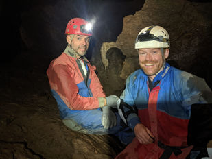 Caving men in cave cavern smiling.