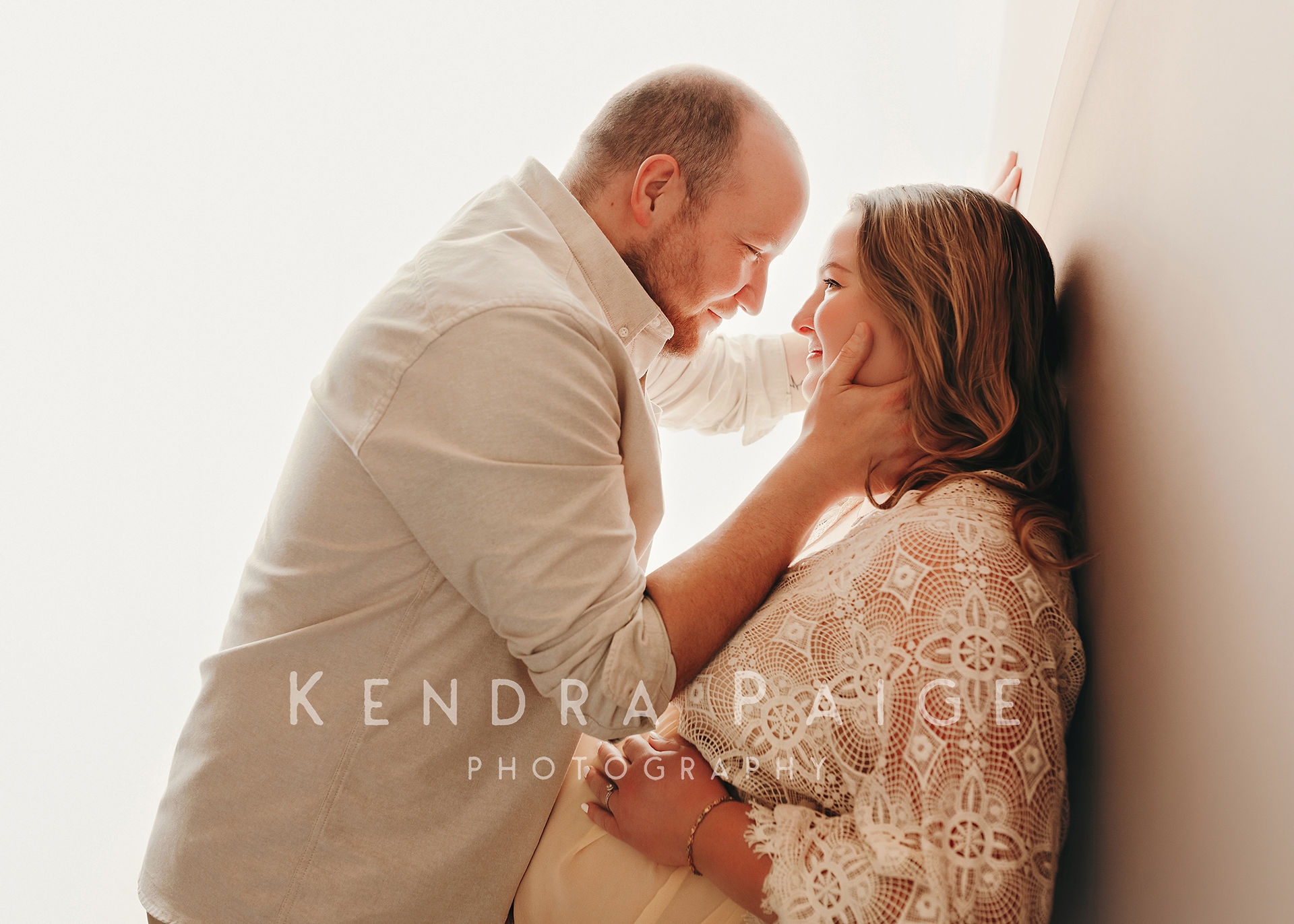 husband holding wife's face while leaning against a wall 