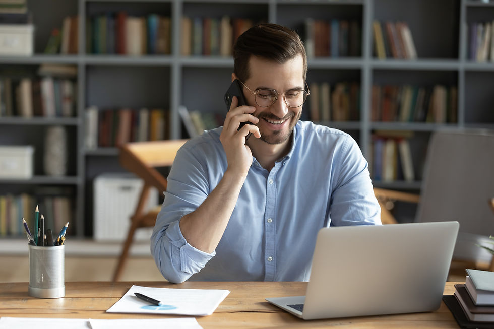Smiling businessman wearing glasses talking on phone, sitting at desk with laptop, friendl