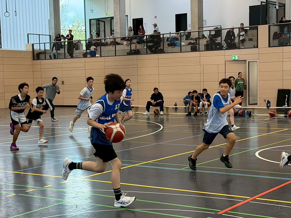 体育館で男子バスケットボールの試合。青と黒のユニフォームの選手が走り、観客が2階席から見守る。