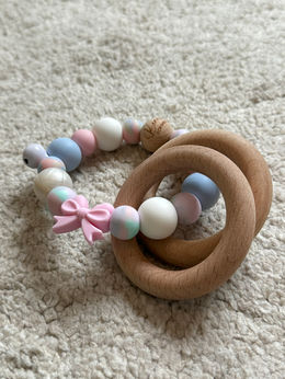 Pastel bijtring met roze, blauw en wit en tie dye kraal. Afgewerkt met strik en dubbele ringen. Uniek babycadeau meisje.
