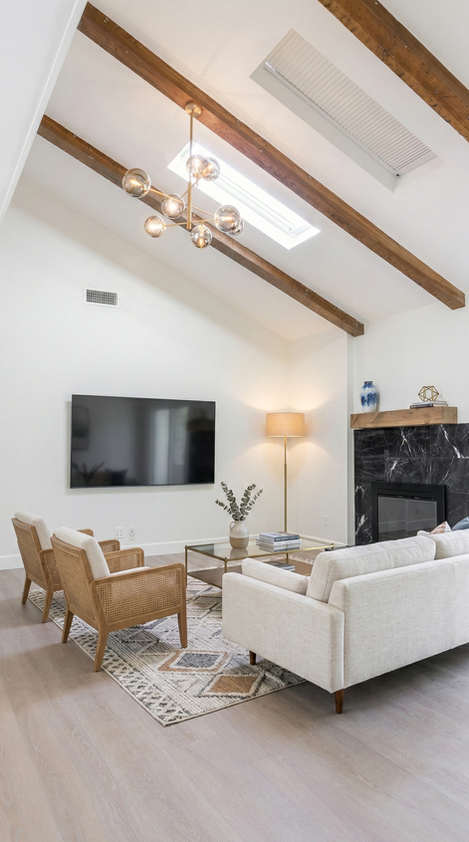 Bright modern minimalist living room with a vaulted ceiling, exposed wood beams, a modern glass globe chandelier, and a black marble fireplace.